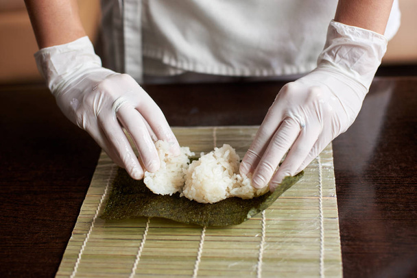 Close-up weergave van het proces ter voorbereiding van rollende sushi. Nori en witte rijst op bamboe mat. Chef's handen aanraken rijst. Chef-kok begint koken sushi. - Foto, afbeelding