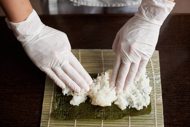Close-up weergave van het proces ter voorbereiding van rollende sushi. Nori en witte rijst op bamboe mat. Chef's handen aanraken rijst. Chef-kok begint koken sushi. - Foto, afbeelding