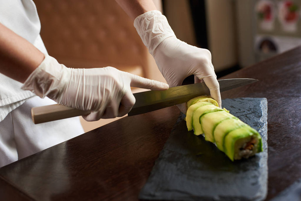 Close-up weergave van het proces ter voorbereiding van rollende sushi. Chef-kok is snijden roll op de zwarte stenen plaat - Foto, afbeelding