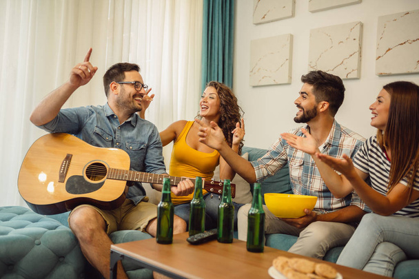 Grupo de jóvenes amigos felices con guitarra divirtiéndose y bebiendo cerveza en el interior
 - Foto, imagen