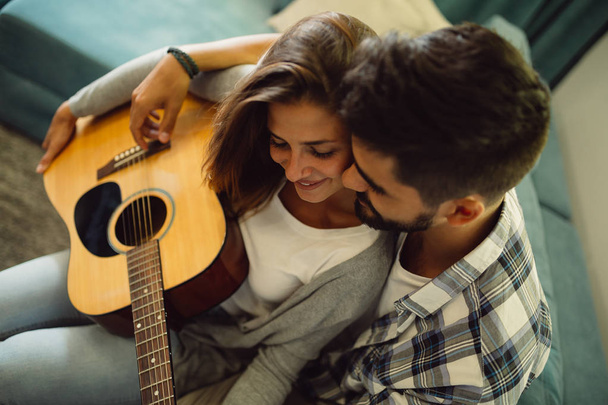 Teaching her to play guitar. Handsome young bearded man teaching his girlfriend to play guitar - Photo, Image