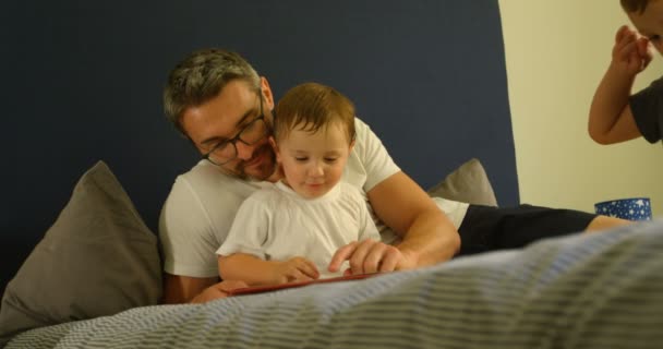Father and son reading book on bed at home 4k - Felvétel, videó