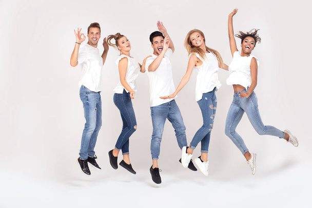 Group of young multi-ethnic attractive people wearing white shirts, smiling and having fun together, jumping in studio. - Foto, Imagem