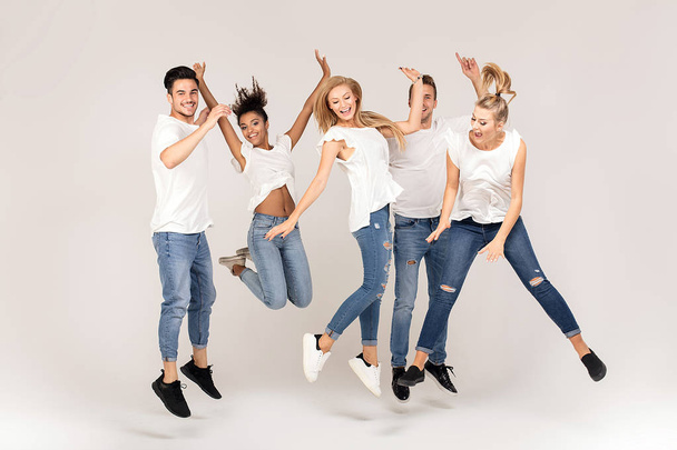 Group of young multi-ethnic attractive people wearing white shirts, smiling and having fun together, jumping in studio. - Foto, imagen