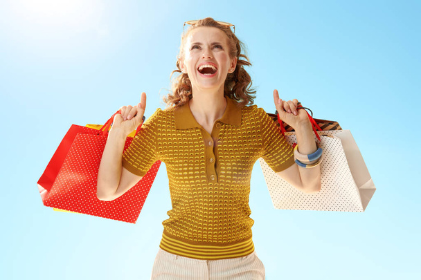 happy trendy woman with shopping bags pointing up against blue sky - Foto, Imagen