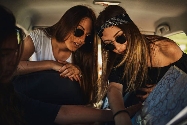 Three young women looking at map and having fun on roadtrip. - Фото, зображення