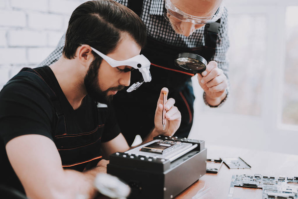 Two Men Repairing Hardware Equipment in Workshop. Repair Shop. Worker with Tools. Computer Hardware. Young and Old Workers. Modern Devices. Digital Device. Man in Glasses. Electronic Devices Concept. - Photo, Image