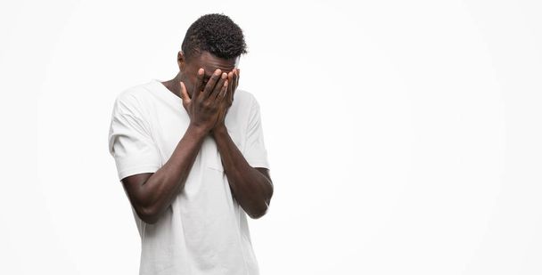 Молодой африканский американец в белой футболке с грустным лицом, прикрывающим лицо руками во время плача. Концепция депрессии
. - Фото, изображение