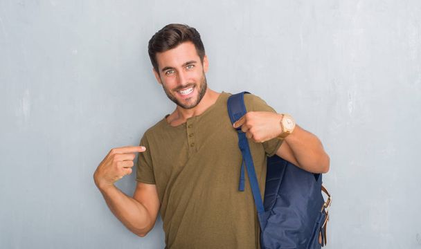 Красивий туристичний молодий чоловік над сірою гранжевою стіною в рюкзаку впевнено виглядає з посмішкою на обличчі, вказуючи на себе пальцями гордим і щасливим
. - Фото, зображення