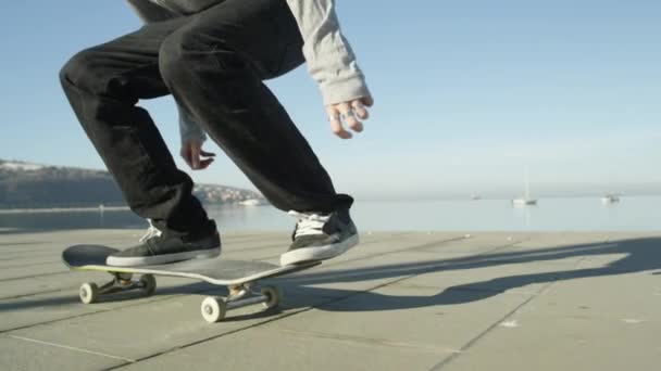 Zpomalený pohyb, Close Up, Dof: K nepoznání skateboardista skateboardingu a skákání 360 flip trik na promenádě podél oceánu v slunné léto. Skateboardista koni skateboard skákání kickflip trik - Záběry, video