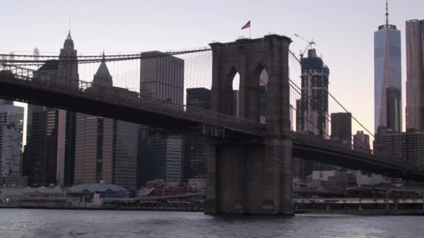 Close Up, lage hoekmening: Sightseeing twilight cruise langs de East River onder de Brooklyn Bridge naar iconische skyline van Downtown Manhattan. Gloed van zonsondergang op beroemde wolkenkrabbers en condominium flats - Video