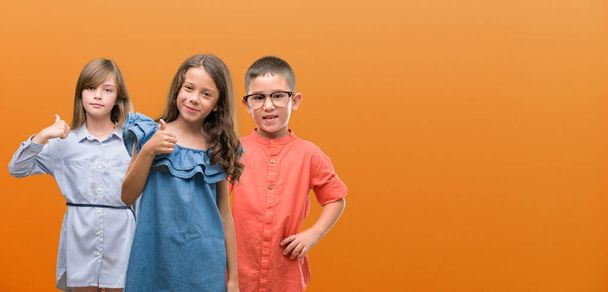 Group of boy and girls kids over orange background happy with big smile doing ok sign, thumb up with fingers, excellent sign - Photo, Image