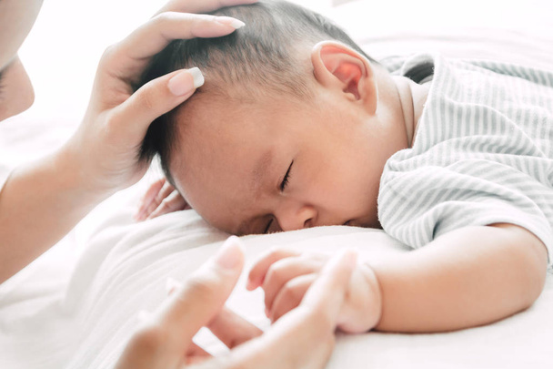 Mutter hält schlafendes Baby an der Hand auf weißem Bett - Foto, Bild