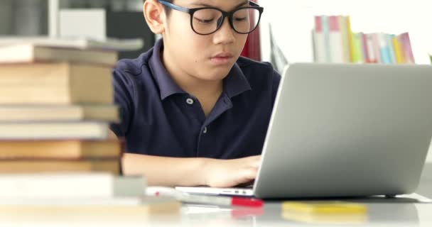 Asijské teen boy waring brýlí a používaný přenosný počítač doma, roztomilý chlapec dělá úkoly s vážnou tváří. - Záběry, video