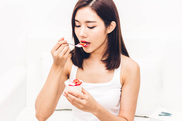 Mujer comiendo yogur con fresa fresca mientras se relaja en el sofá en casa.
 - Foto, imagen