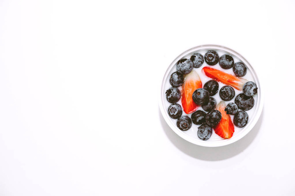 Mísa z jogurtu a míchaným ovocem borůvky s jahodami na bílém pozadí - Fotografie, Obrázek