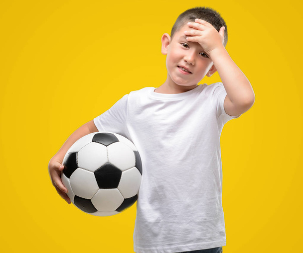 Koyu saçlı küçük çocuk futbol topu elle kafasına, utanç ve sürpriz yüz ile şok vurguladı ile oynarken öfkeli ve sinirli. Korku ve hata için üzgün. - Fotoğraf, Görsel