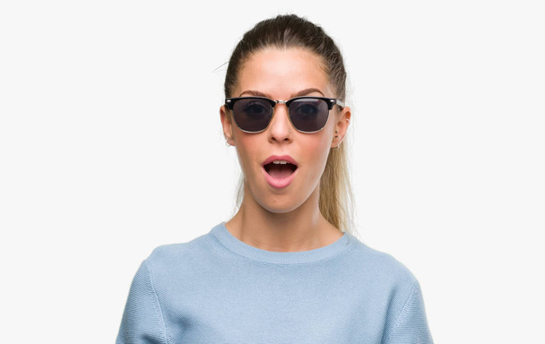 Mooie jonge vrouw dragen zonnebril en paardenstaart bang in schok met een verrassing gezicht, bang en opgewonden met angst expressie - Foto, afbeelding