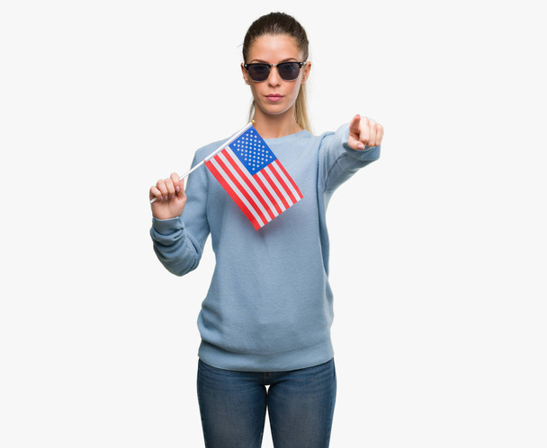 Piękna młoda kobieta trzyma wskazując palcem do aparatu i do Ciebie, znak ręką gest pozytywny i pewnie z przodu flaga Usa - Zdjęcie, obraz