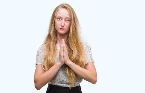 Blonde teenager woman wearing moles shirt begging and praying with hands together with hope expression on face very emotional and worried. Asking for forgiveness. Religion concept. - Fotó, kép