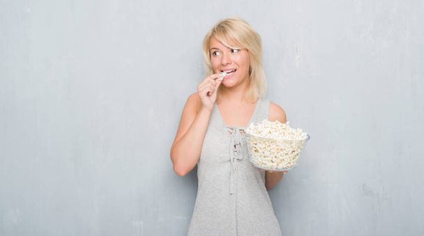 Adulto donna caucasica oltre grunge muro grigio mangiare pop corn con un'espressione fiduciosa sul viso intelligente pensando grave
 - Foto, immagini