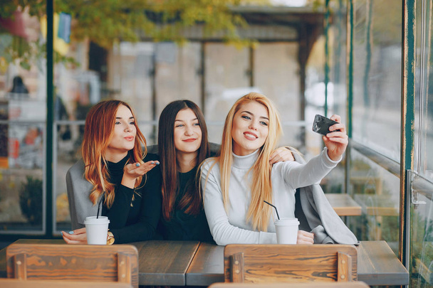 three girls sitting in a cafe at the table, drinking coffee and taking pictures on the phone - Foto, afbeelding