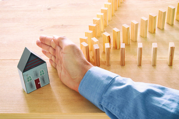 concept image of real estate insurance and protection. man hands blocking the domino effect, saving a small house - Fotografie, Obrázek