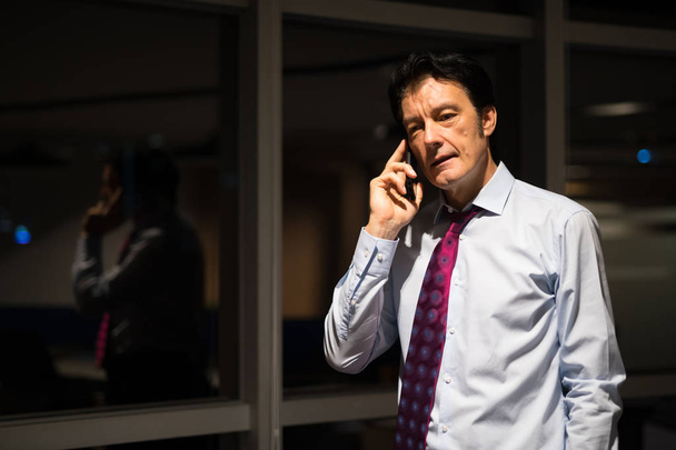 Mature Businessman In Office At Night Talking On Mobile Phone - Fotografie, Obrázek