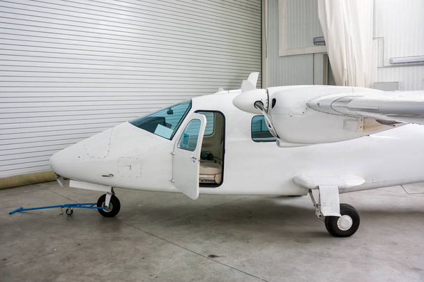 High-winged twin-engined light aircraft with open door in hangar - Valokuva, kuva