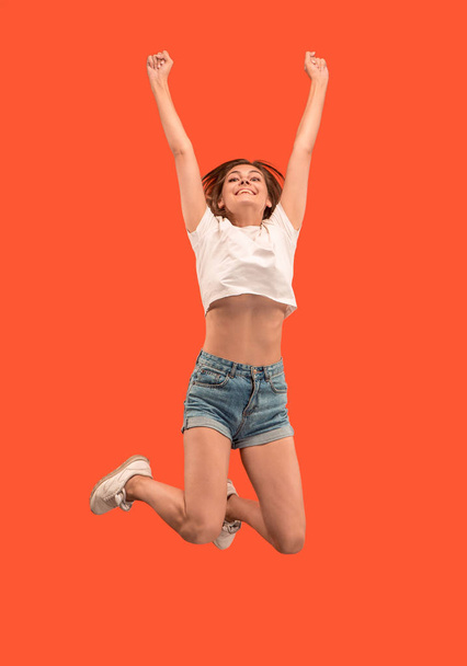 Freedom in moving. Pretty young woman jumping against orange background - Foto, Imagen