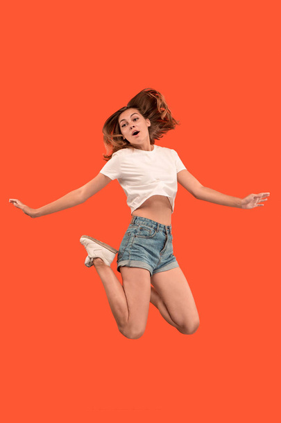 Freedom in moving. Pretty young woman jumping against orange background - Photo, Image