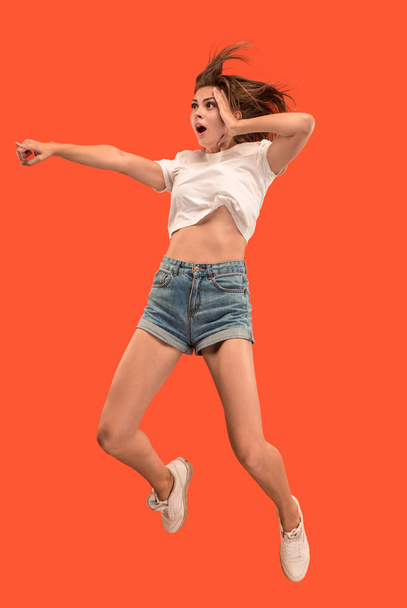 Freedom in moving. Mid-air shot of pretty happy young woman jumping and pointing by finger against orange studio background. Runnin girl in motion or movement. Human emotions and facial expressions - Fotografie, Obrázek