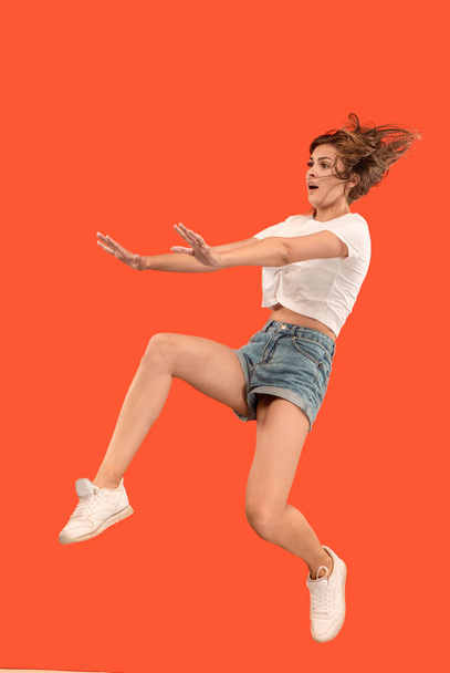 Svoboda v pohybu. Hezká mladá žena skákání proti oranžové pozadí - Fotografie, Obrázek