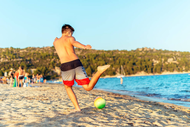 Onbezorgd kind spelen met voetbal op zand tijdens zomervakantie - Foto, afbeelding