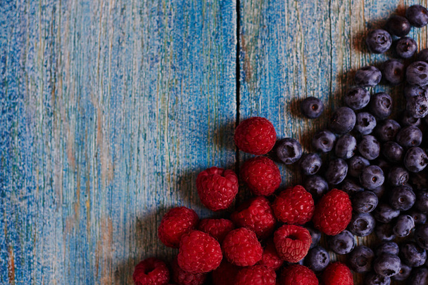 Группа спелых сочных органических ягод на голубом деревенском столе. Вкусный натуральный вегетарианский ингредиент. Черника с малиной. Здоровые летние фрукты, антиоксиданты. Вид сверху с пространством для копирования
. - Фото, изображение
