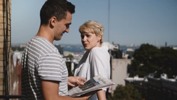 New York, juli 2018. Jonge man en vrouw staan samen met Kranten, genieten van praten op kleine zonnig balkon. - Video