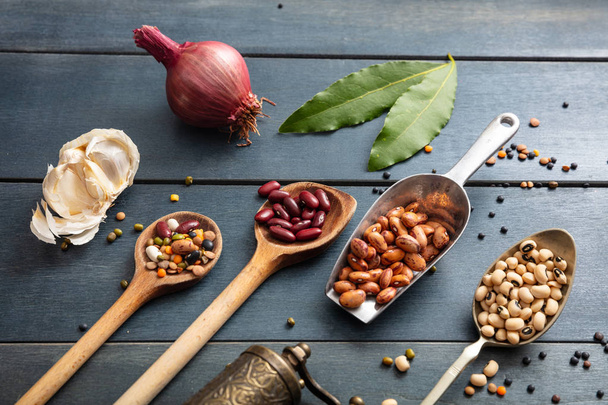 Healthy diet concept. Top view of flat lay of assortment of legumes on black wooden tabletop background, in scoop and ladles and grater. - Valokuva, kuva