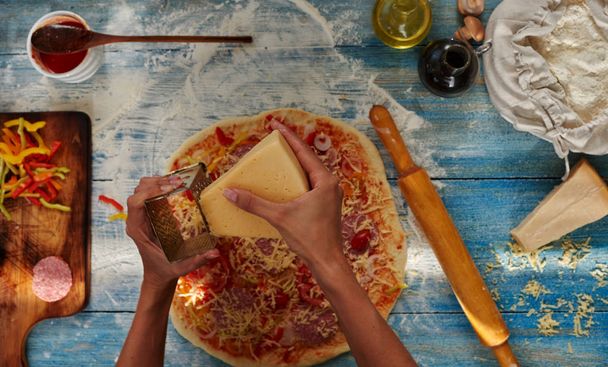 Raw pizza ingredients on wooden table. Preparing classical pizza. Adding cheese to pizza. Italian food homemade concept. - 写真・画像