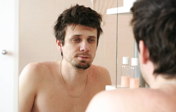Tired man who has just woken up looks at his reflection in the mirror and surprised. - Foto, Imagem