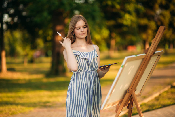 Rubia chica de pelo en el vestido de dibujo de un cuadro en el parque
 - Foto, Imagen