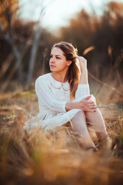 girl is sitting in the field on the sunset background. - Foto, Imagen