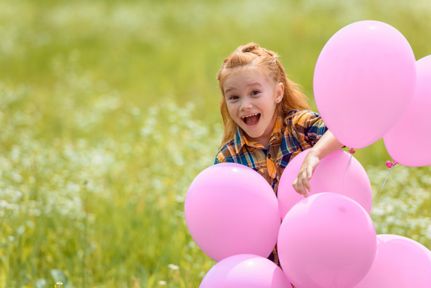 Portret van vrolijke schattig kind met roze ballonnen in zomer veld - Foto, afbeelding
