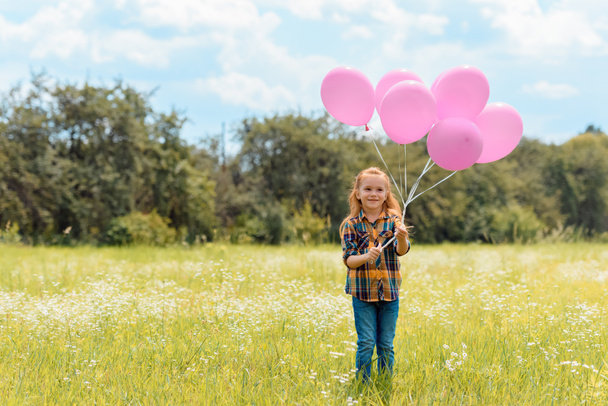 усміхнена дитина з рожевими кульками, що стоять на літньому полі
 - Фото, зображення