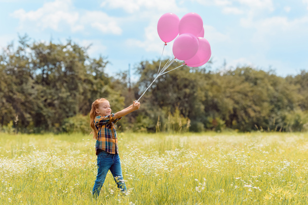 adorable child with pink balloons standing in summer field - Фото, зображення