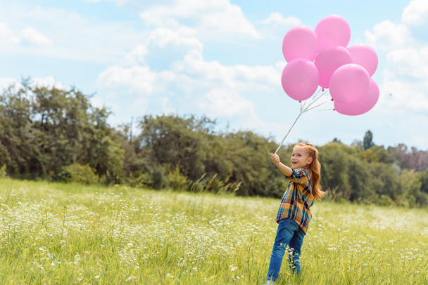 adorable child with pink balloons standing in summer field with blue sky on background - Photo, Image
