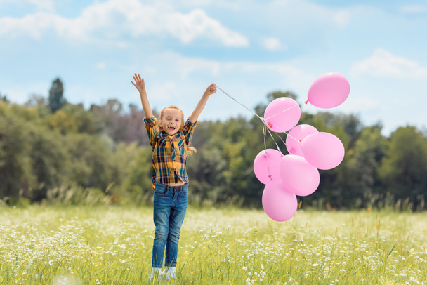happy child with pink balloons in summer field - Fotó, kép