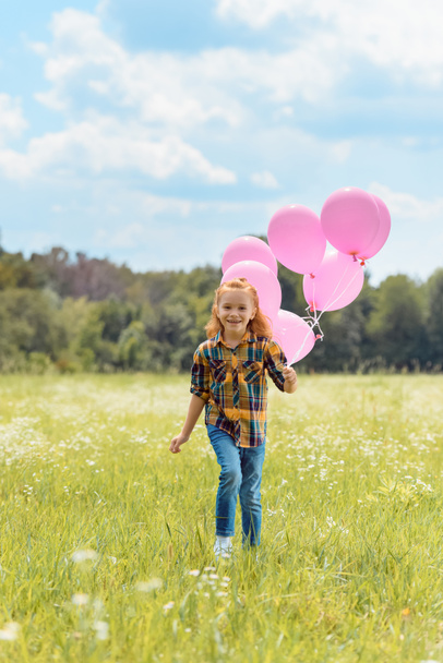 cheerful kid with pink balloons in hand running in meadow - Fotó, kép