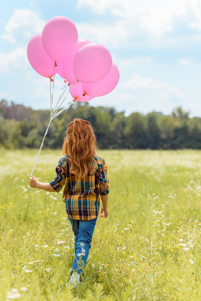 back view of child with pink balloons walking in summer field - 写真・画像