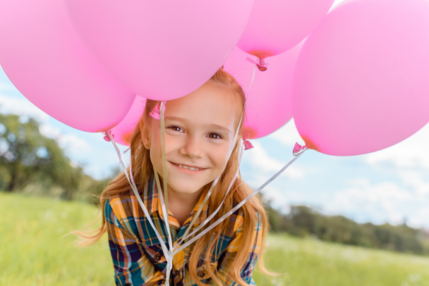 Portret van schattig kind met roze ballonnen kijken camera in zomer veld - Foto, afbeelding