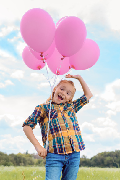 low angle view of cute child with pink balloons in summer field with blue cloudy sky on background - Photo, Image